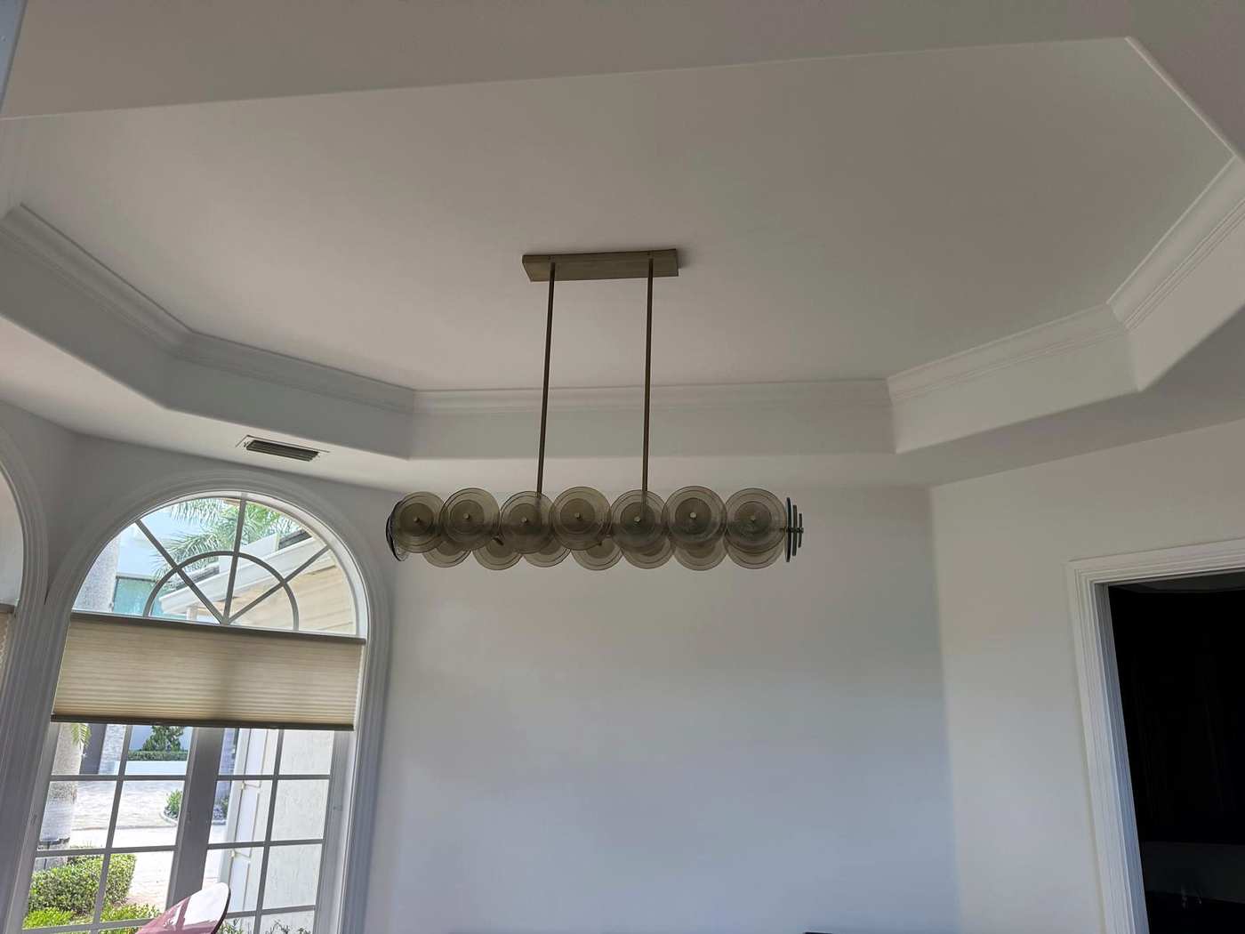 Linear chandelier with smoked glass discs in a tray ceiling, an arched window behind