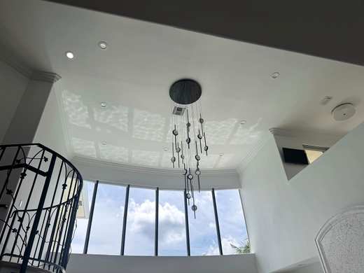 Modern chandelier hanging in a two-story stair hall with a wall of windows