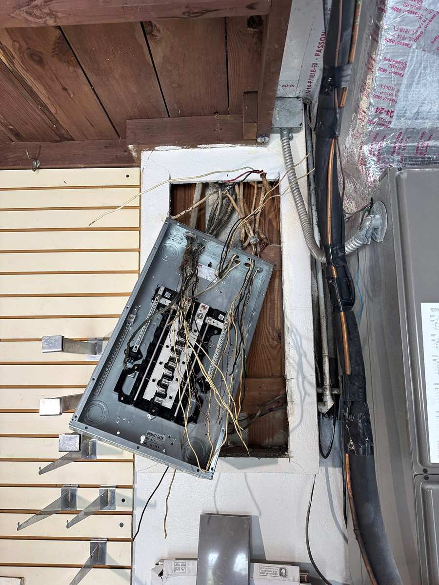 Old panel tilted out of its wall opening, its wires still attached
