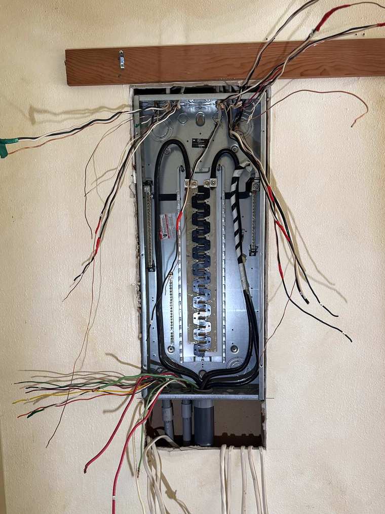 New panel enclosure set into a wall under a wood strip, circuit wires pulled in and not yet connected