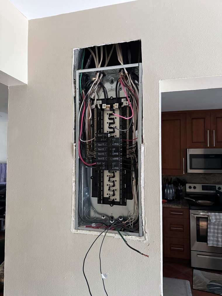 Panel set into a wall beside a kitchen, breakers in and wiring connected, cover off