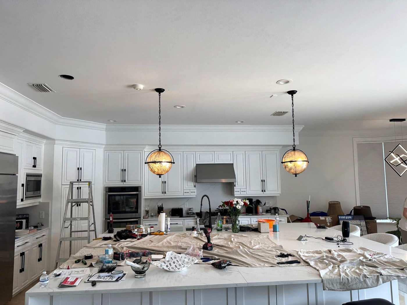 Two globe pendants over a kitchen island during an install, drop cloths on the counter