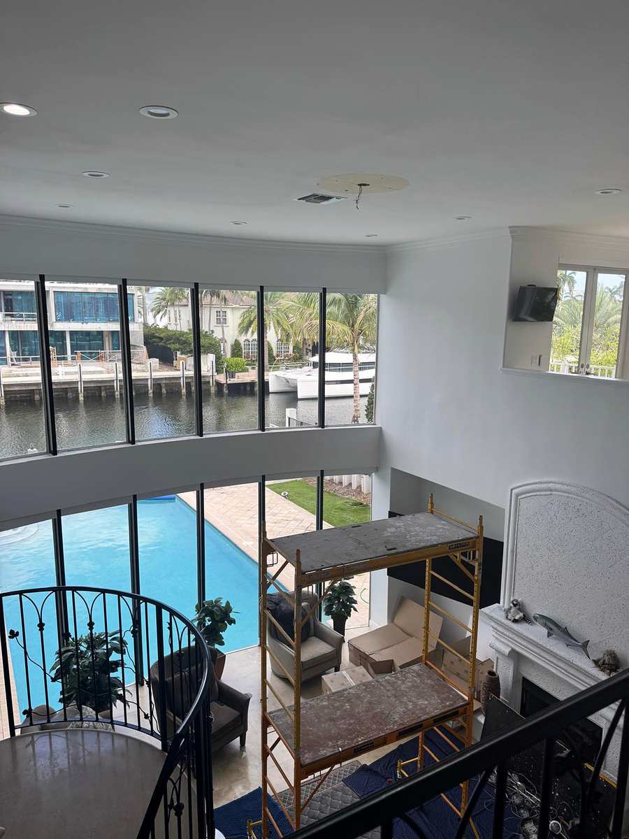 Double height living room with recessed lights and scaffolding set up, pool and canal through tall windows