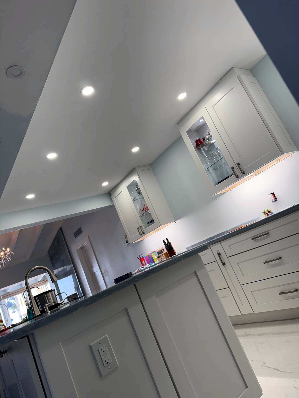 Recessed lights in a kitchen ceiling above lit glass-front cabinets
