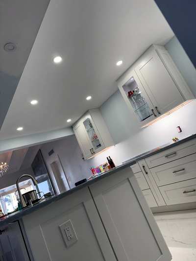 Recessed lights in a kitchen ceiling above lit glass-front cabinets