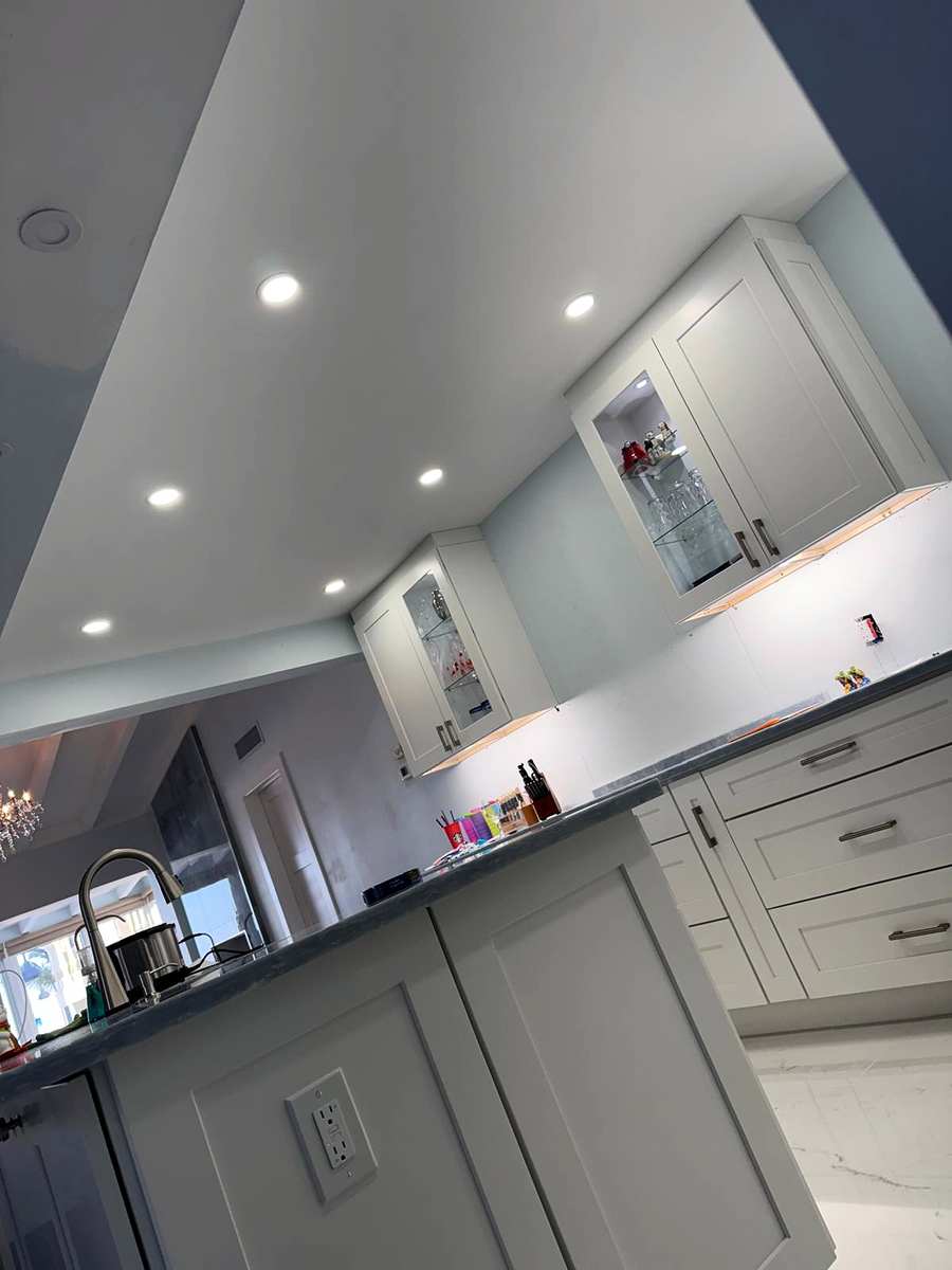 Recessed lights in a kitchen ceiling above lit glass-front cabinets