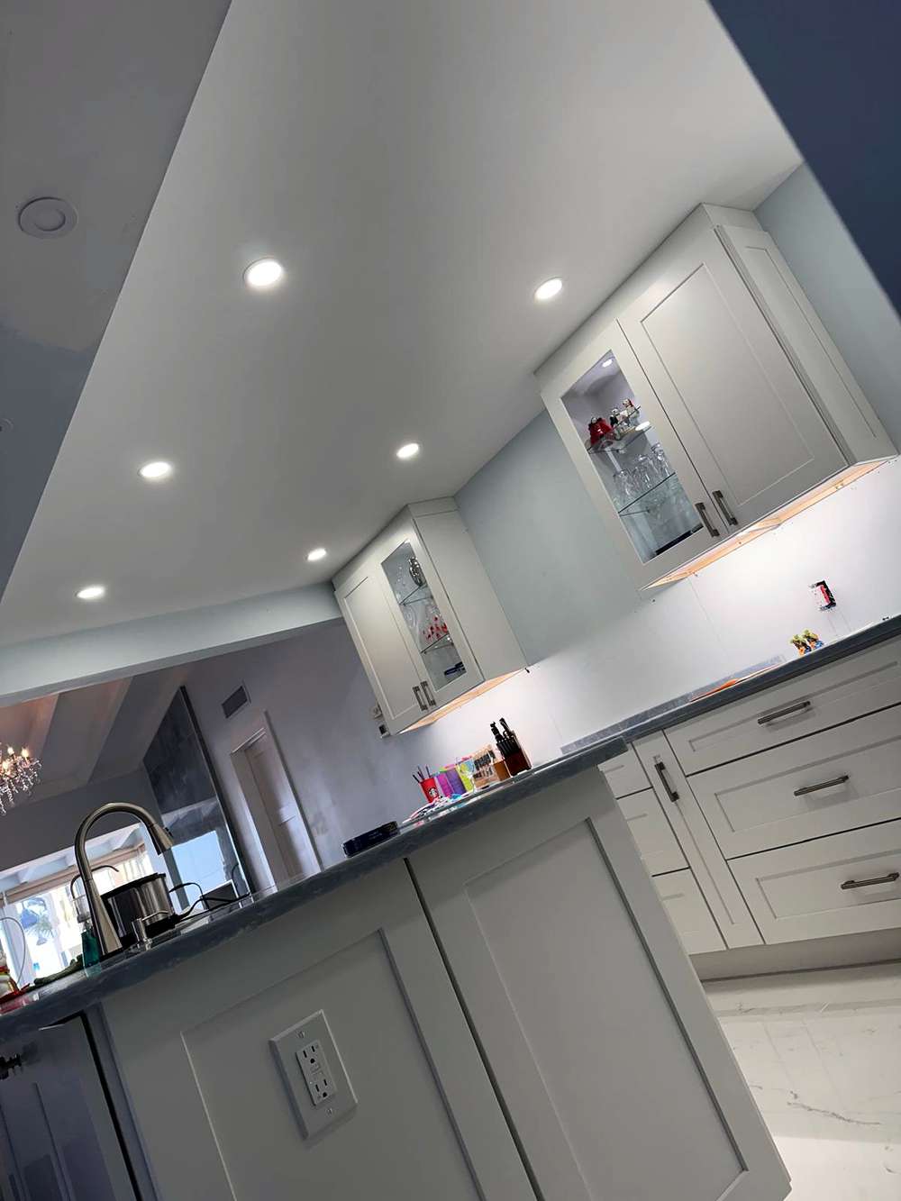 Recessed lights in a kitchen ceiling above lit glass-front cabinets