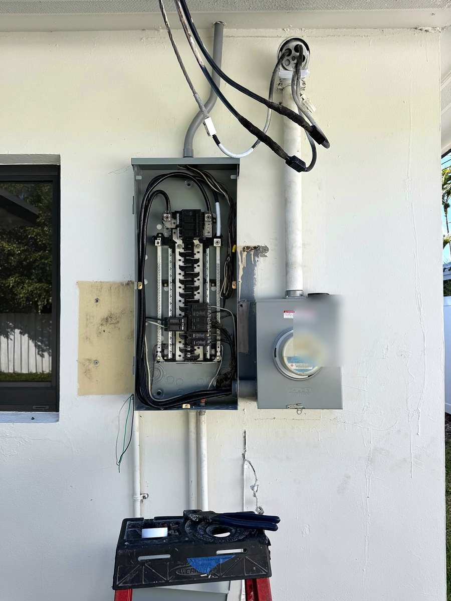 Outdoor panel open beside the meter on a white wall, breakers and wiring visible