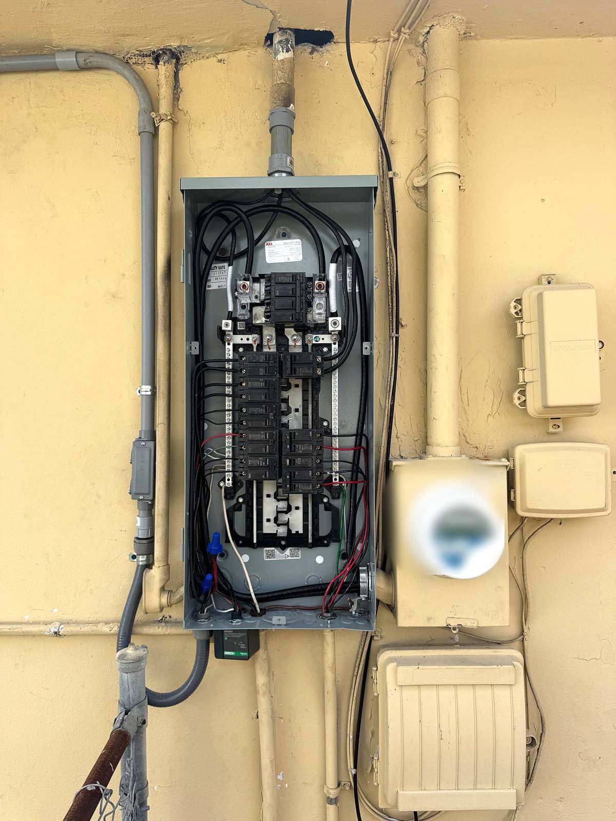 Outdoor panel with the cover off on a yellow stucco wall, next to the meter