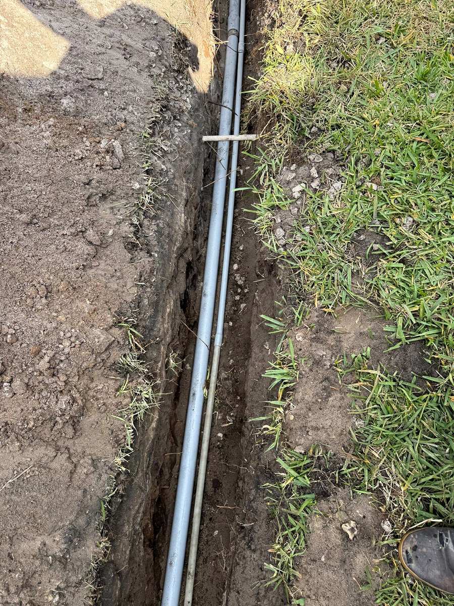 Gray conduit laid in an open trench across a lawn